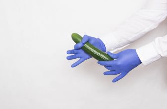 The doctor in medical gloves holds a cucumber in his hands, the concept of increasing the penis with the help of massage techniques and techniques, white background