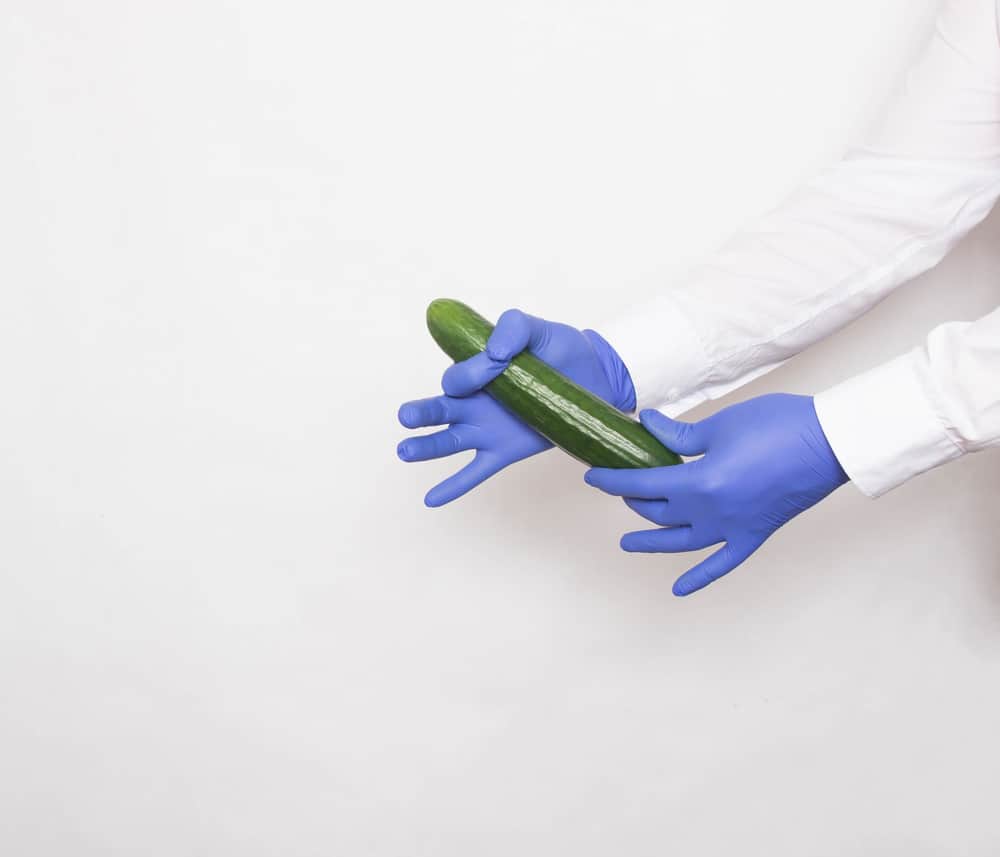 The doctor in medical gloves holds a cucumber in his hands, the concept of increasing the penis with the help of massage techniques and techniques, white background